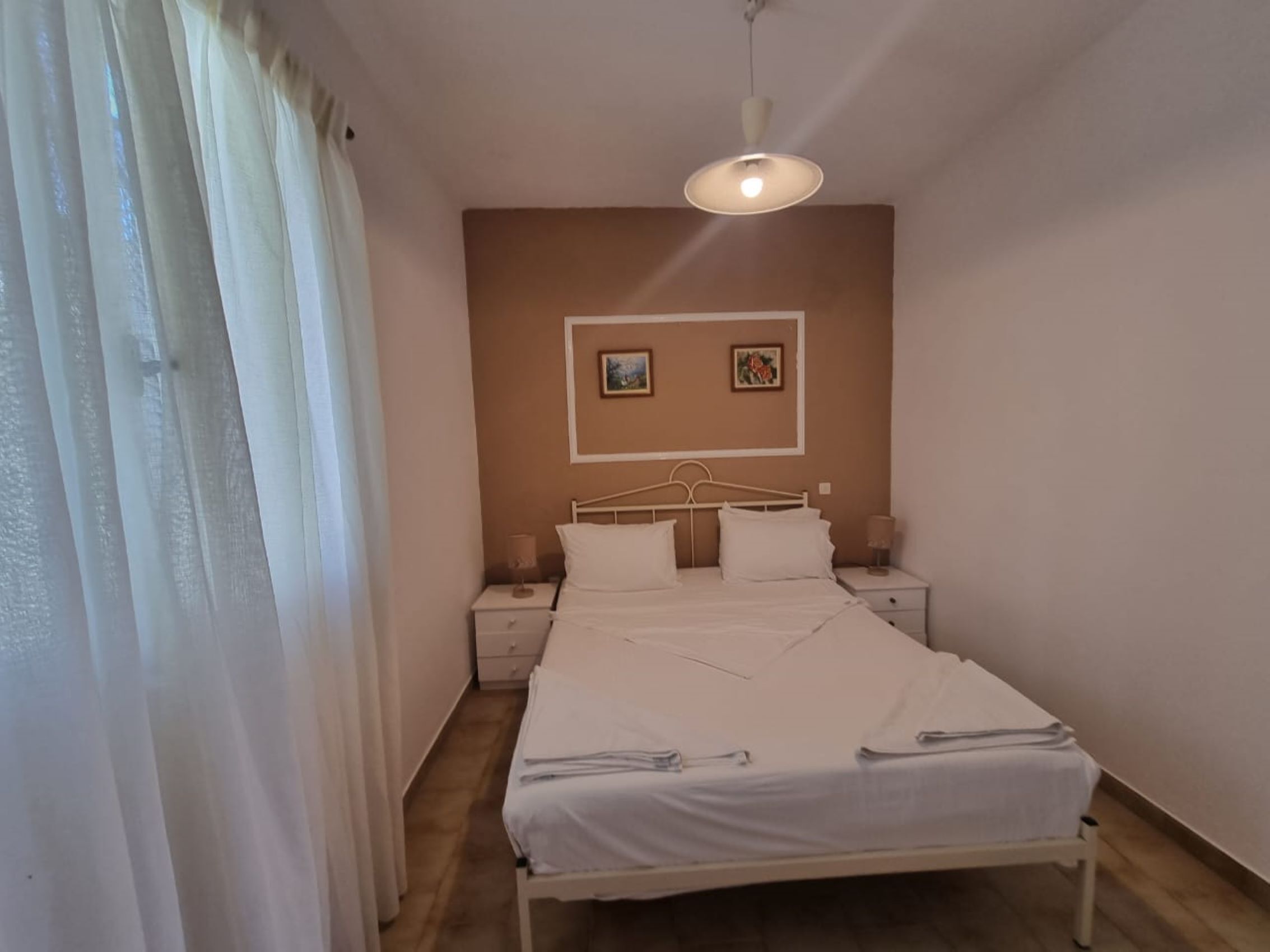 A bedroom with a bed, two bedside tables, a ceiling light, and two framed pictures on the wall.