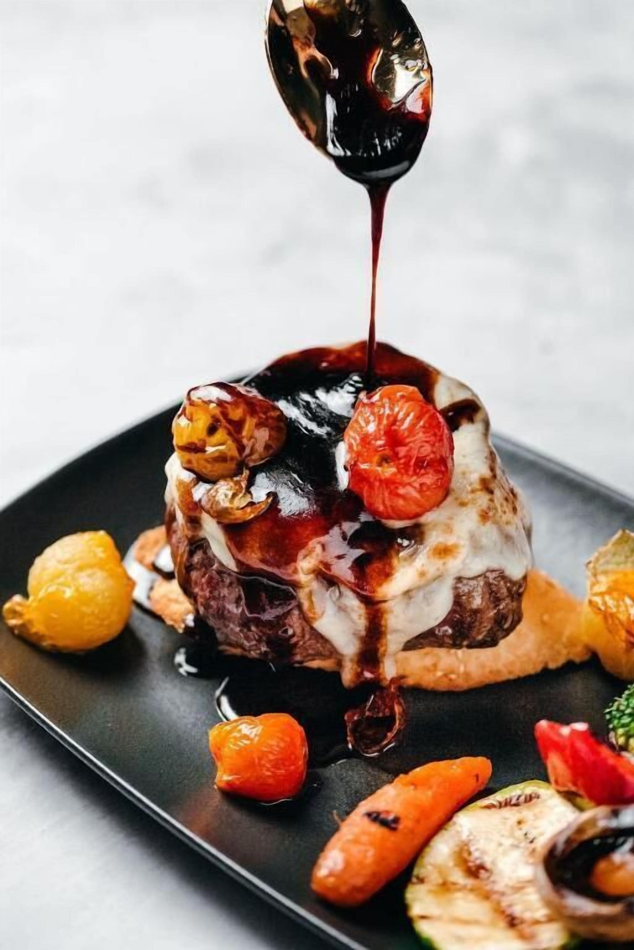 A dessert with a dark sauce being poured over it, accompanied by grilled vegetables.