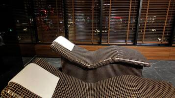 A modern lounge area with a curved, mesh-patterned sofa and a matching ottoman, set against a cityscape view through large windows.