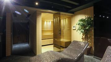 A modern spa room with a glass-enclosed sauna, a potted plant, and a seating area with patterned cushions.