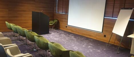 Ein Konferenzraum mit Projektionsleinwand, einer Whiteboard und Reihen von Stühlen.