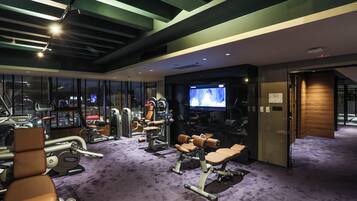 Une salle de sport moderne équipée de divers appareils d’exercice, d’un grand écran de télévision et d’un sol recouvert d’une moquette violette.