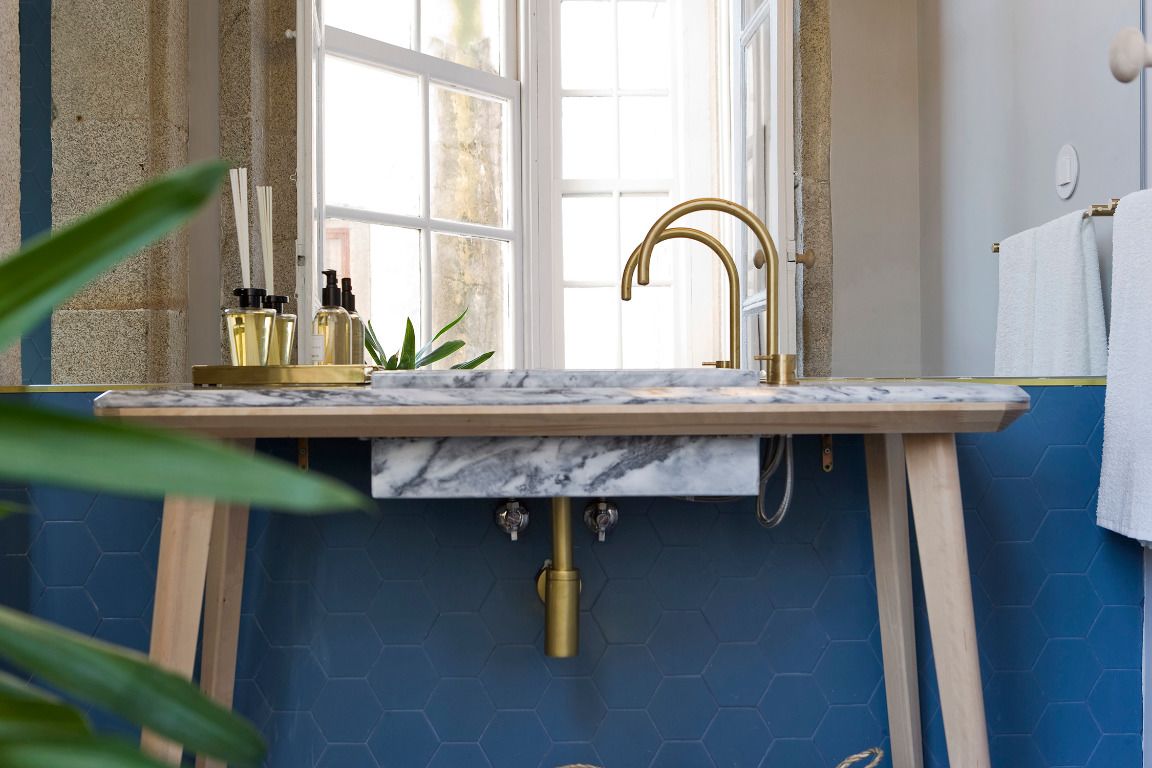 A bathroom with a marble sink, gold fixtures, and a blue hexagonal tile wall.