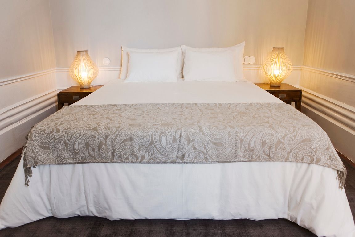Uma cama bem arrumada com colcha estampada e duas luminárias nas mesas de cabeceira de madeira.