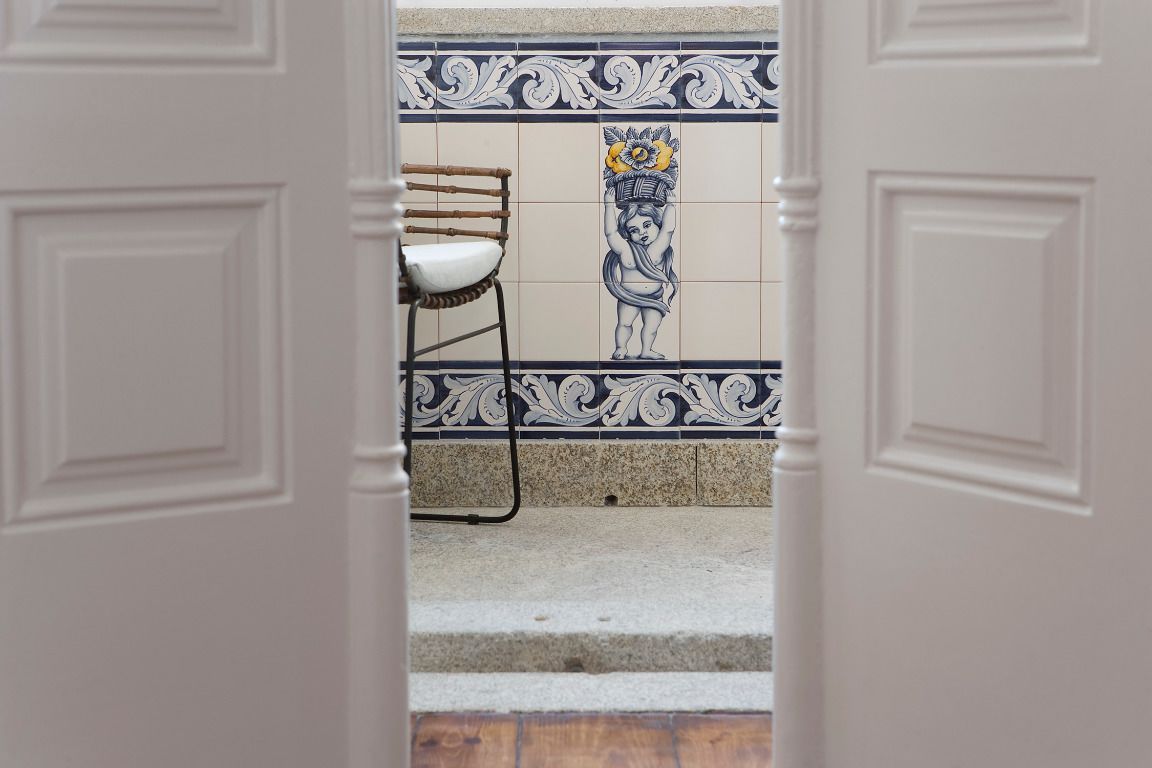 A view through an open door into a room with a tiled wall featuring a decorative pattern and a chair.