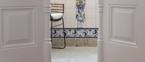 A view through an open door into a room with a tiled wall featuring a decorative pattern and a chair.