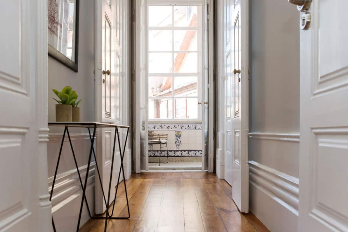 A hallway with a wooden floor, white doors, and a tiled entryway.