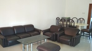 Uma sala de estar com um sofá de couro marrom, uma mesa de centro de vidro e um banquinho combinando.