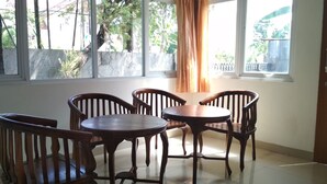 A room with a dining table and four chairs, large windows with curtains, and a view of trees and buildings outside. - De Sutami Pasteur Villa by HouseinBandung (Bandung)