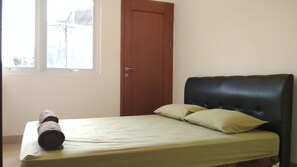 Simple room with a single bed, featuring a headboard and pillows, and a window for natural light.