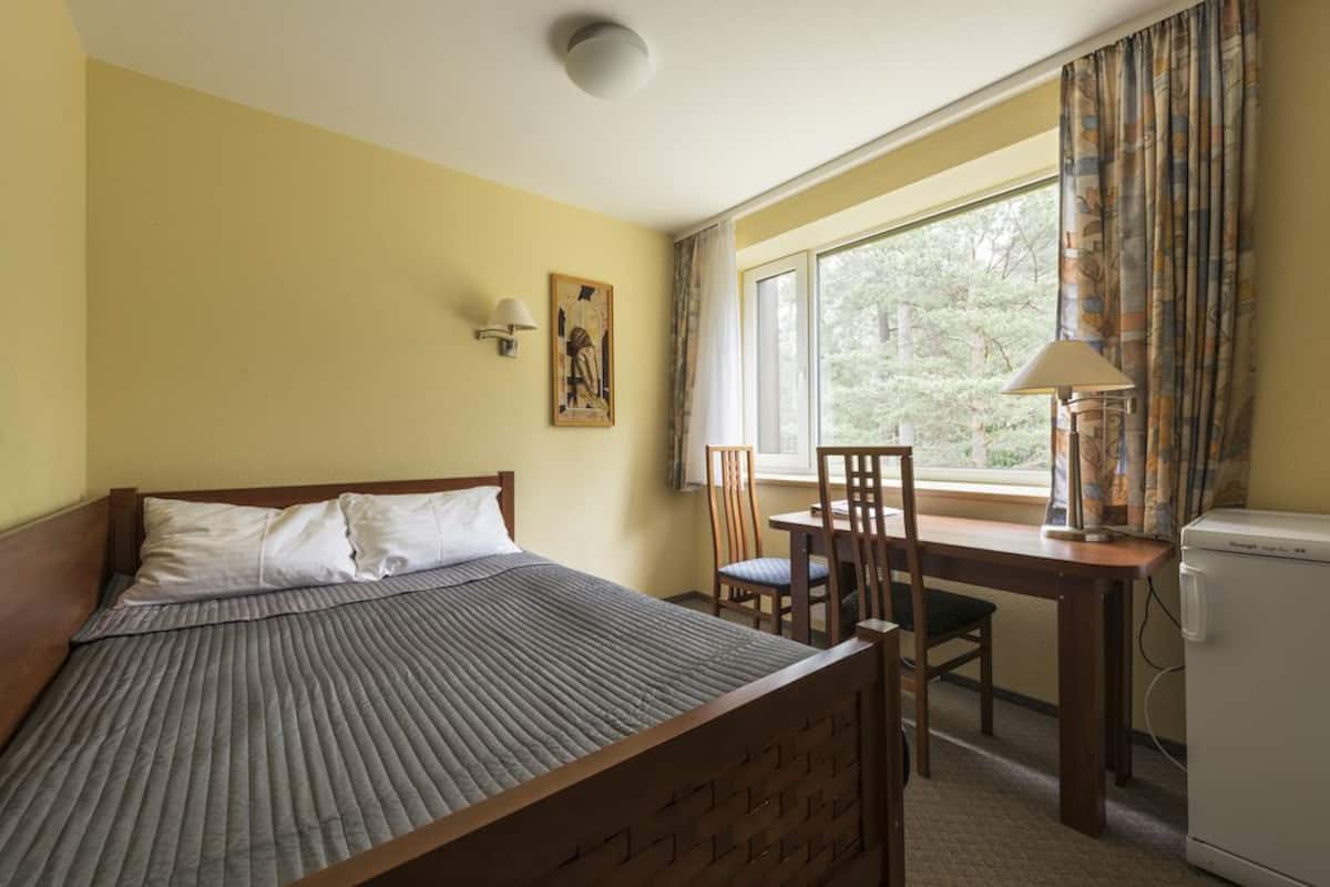 A bedroom with a bed, a desk, chairs, a lamp, and a window with curtains.