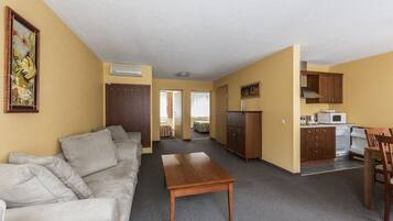 A compact living space with a sofa, a wooden table, a kitchenette, and a door leading to another room.