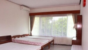 A room with two single beds, a wooden headboard, a window with sheer curtains, and a small bedside table.