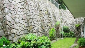 A stone wall with a garden area featuring green plants and a paved pathway.