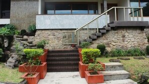 A modern house with a stone facade, a set of stairs leading to a balcony, and potted plants around the entrance.
