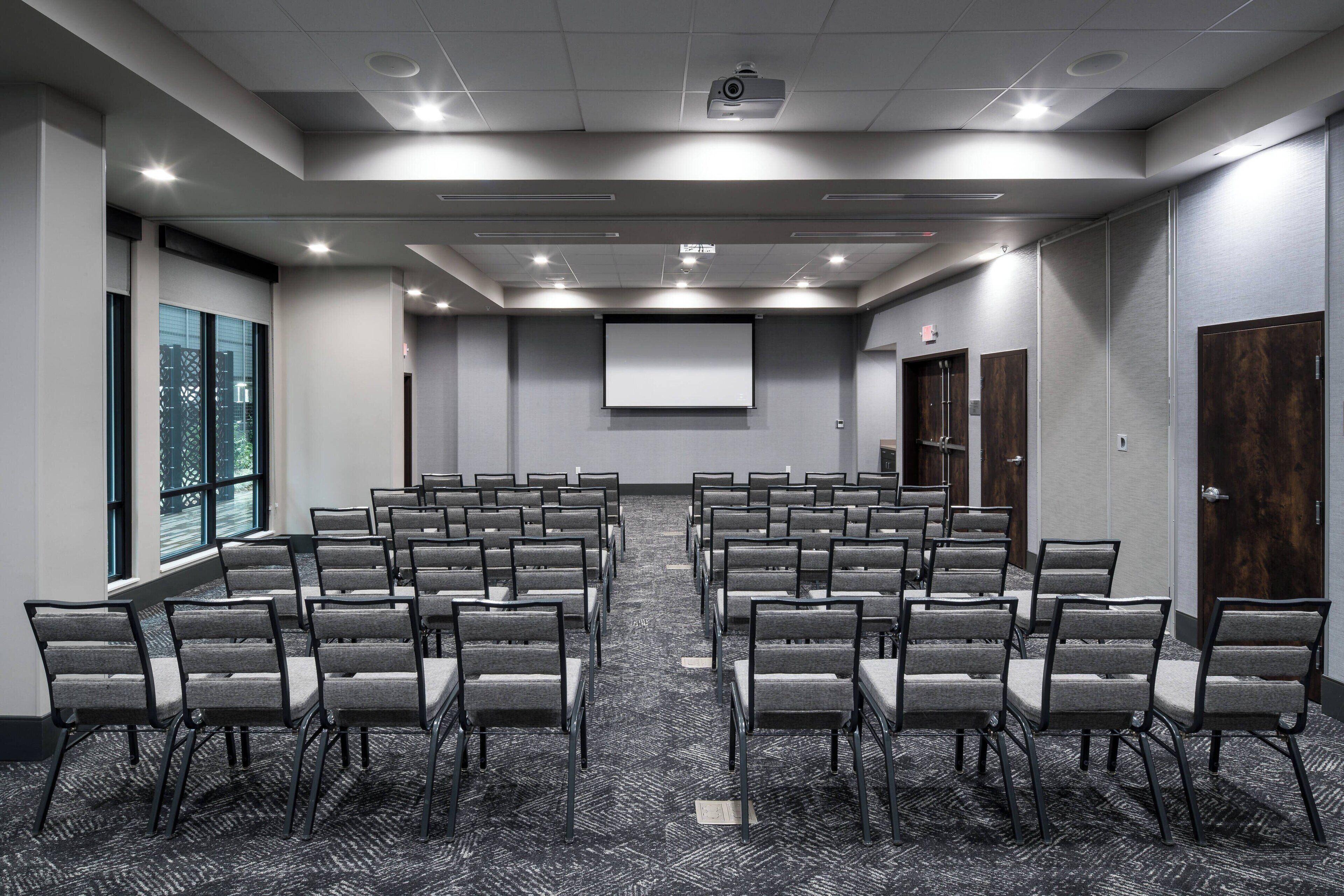 Une salle de conférence avec des rangées de chaises, un écran de projection et une grande fenêtre.