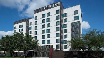 Un hotel de varios pisos con un diseño moderno, que destaca un cartel prominente de 'Courtyard by Marriott' en la parte superior.