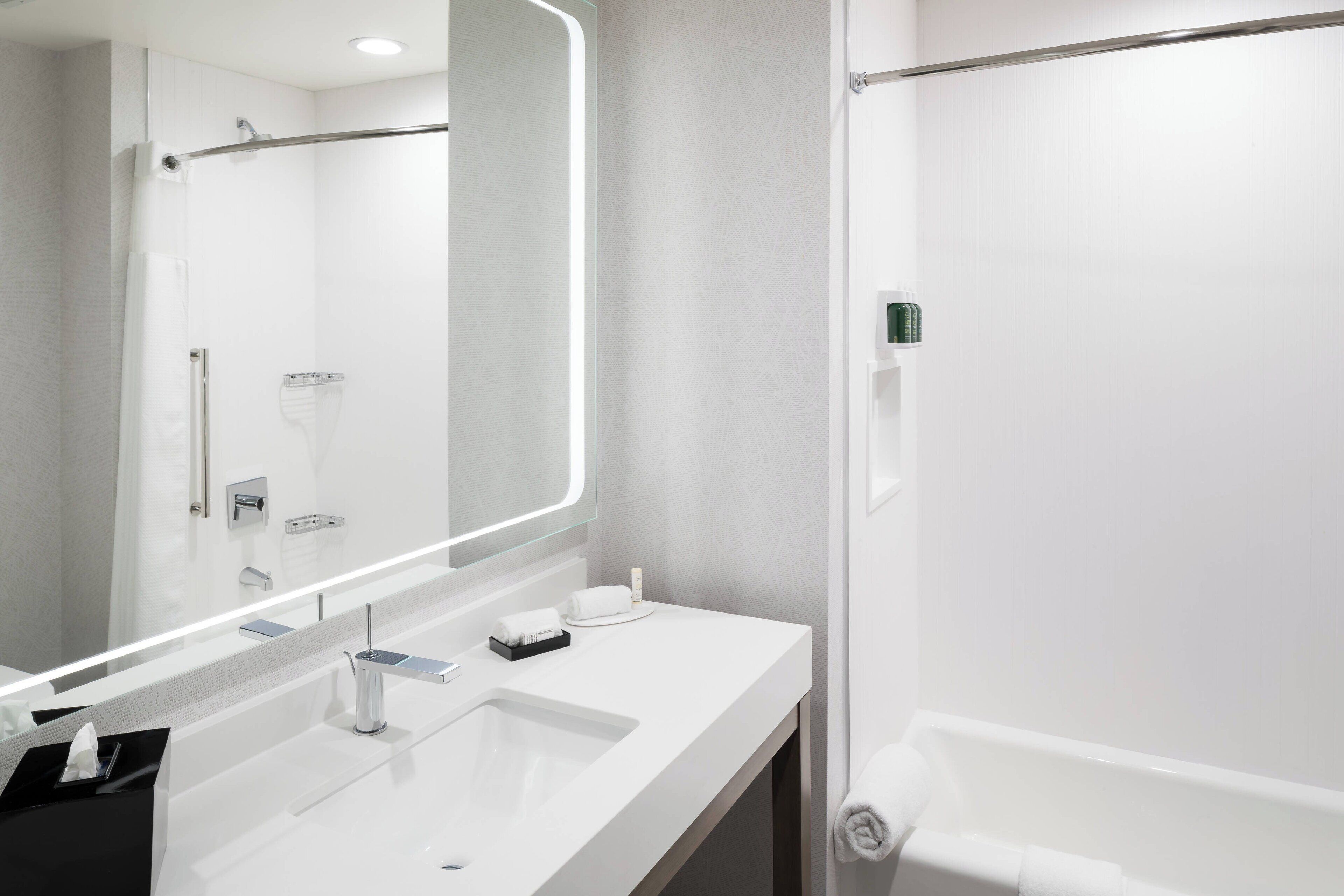 A modern bathroom with a large mirror, a sink, and a shower area.