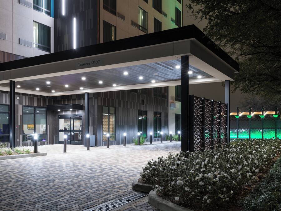Una entrada de hotel moderna con un paseo techado, señalización clara y senderos bien iluminados.