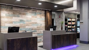 A reception area with two dark wooden reception desks, a wall with a wood plank pattern, and a 'market' sign indicating a food section. - Courtyard by Marriott Houston Heights/I-10 (Houston)