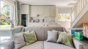 Una sala moderna con un sofá gris, una mesita y una cocina al fondo.