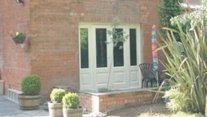Una casa de ladrillo de dos pisos con puerta principal, un pequeño porche y plantas en macetas.