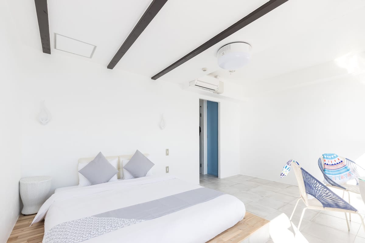 Une chambre moderne avec un grand lit, un petit coin salon avec des fauteuils et une porte donnant sur une autre pièce.