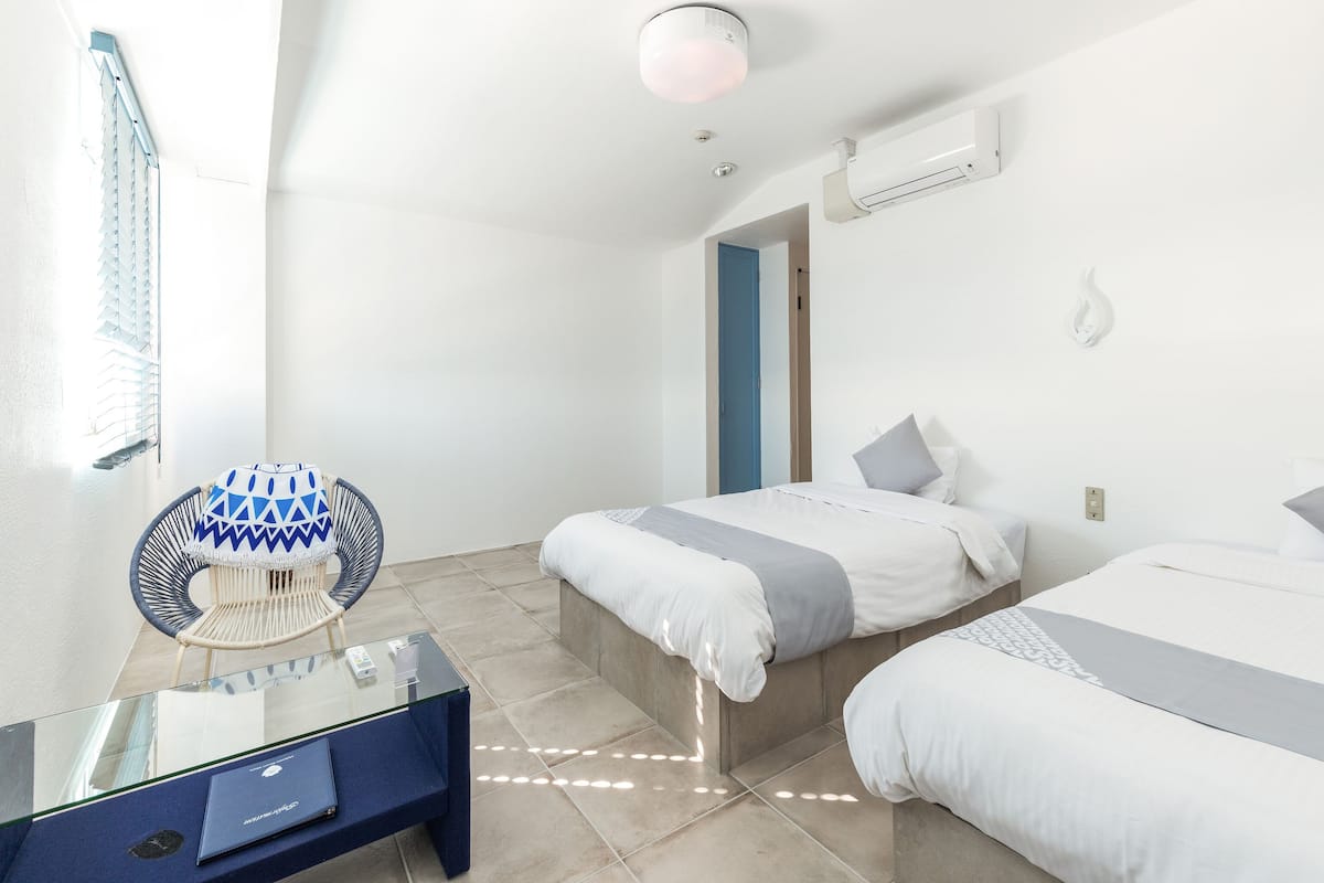 Une chambre d’hôtel moderne avec deux lits, une table en verre, une chaise et un luminaire au plafond.