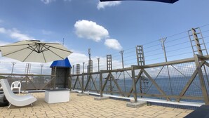 Une terrasse sur le toit offrant une vue sur la mer, un fauteuil de relaxation, une table et un grand parasol.