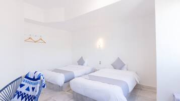Ein Hotelzimmer mit zwei Betten, einem Sessel, einer Wandleuchte und einem Deckenlüfter.