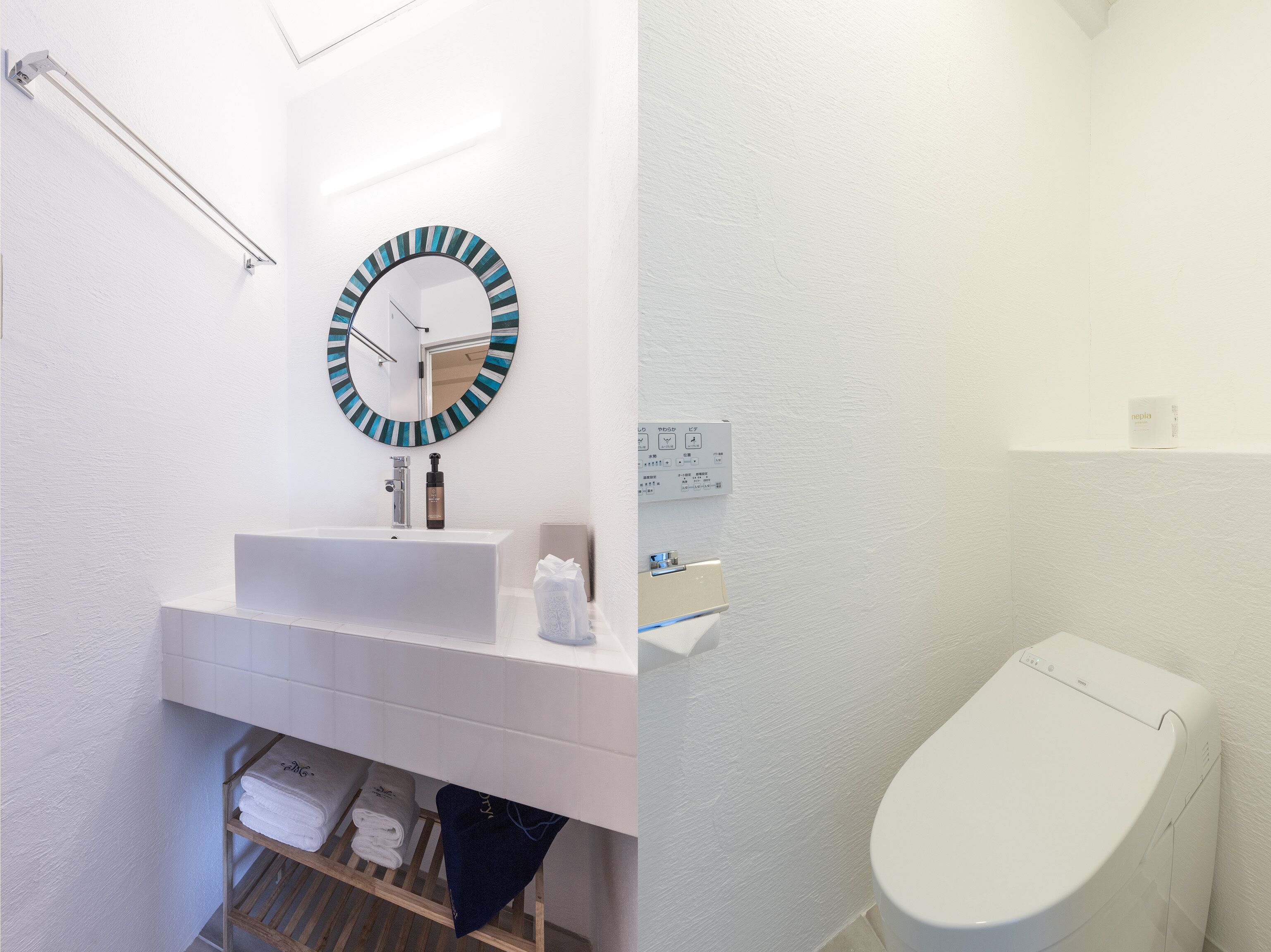 A modern bathroom with a white sink, a round mirror with a blue and black frame, a towel rack, and a toilet.