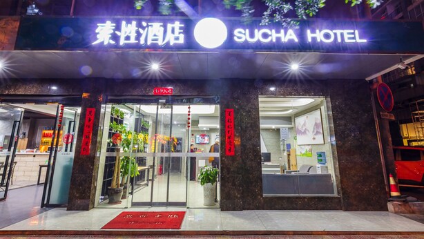 L’entrée d’un hôtel, avec une enseigne indiquant « SUCHA HOTEL » et un paillasson rouge.