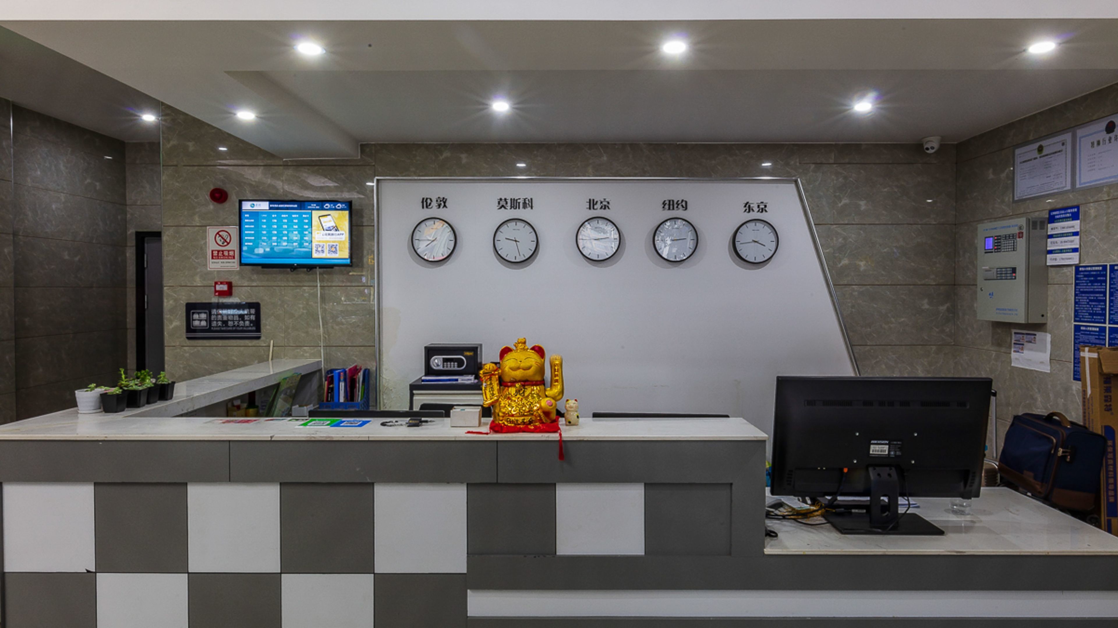 Un mostrador de recepción con una pantalla digital, relojes y una pequeña estatua.
