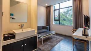 Une chambre d’hôtel moderne dotée d’une grande fenêtre, d’un canapé, d’une petite table, d’un lavabo et d’un miroir.