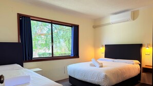 A hotel room with two beds, a large window with curtains, a wall-mounted air conditioner, and bedside lamps.