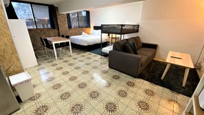 A compact hotel room with a bed, a sofa, a small table, and a TV.