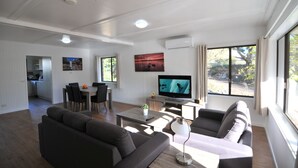 A modern living room with a flat-screen TV, a sofa, a coffee table, and a dining area.