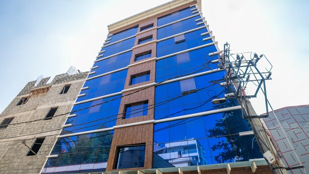 A multi-story building with a modern design, featuring large glass windows and a mix of brick and wood facade elements. - Capital O 36457 Boulevard Madiwala (Bengaluru)