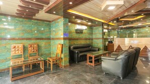 A lobby with a glass coffee table, leather sofa, wooden chairs, and a reception desk. - Capital O 36457 Boulevard Madiwala (Bengaluru)