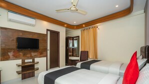 A hotel room with two beds, a flat-screen TV mounted on a wooden panel, a ceiling fan, and a window with curtains. - Capital O 36457 Boulevard Madiwala (Bengaluru)