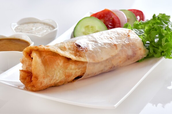 A plate with a wrap, sliced vegetables, and two dipping sauces.