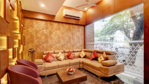 A modern living room with a sectional sofa, a coffee table, and a view of the street through a large window. - Capital O 42226 Pine Tree Signature (Chennai)