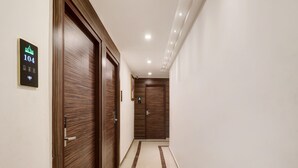 A hallway with wooden doors, a sign indicating room number 104, and a digital elevator control panel. - Capital O 42226 Pine Tree Signature (Chennai)