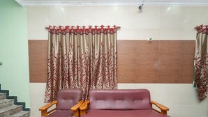 A room with a sofa and a chair, a staircase, and a curtain with a leaf pattern. - OYO 23300 Seabreeze Residency (Puducherry)