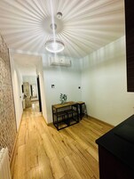 A modern room with a wooden floor, a dining table with chairs, a ceiling light fixture, and an air conditioning unit.