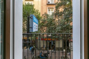 Schild eines Hostels mit blau-weißer Farbgebung, einem Metallzaun und Straßenansicht mit Fußgängern und einem Roller.