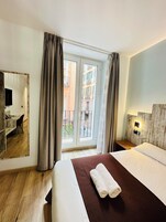 A hotel room with a bed, a desk, and a large window with curtains.