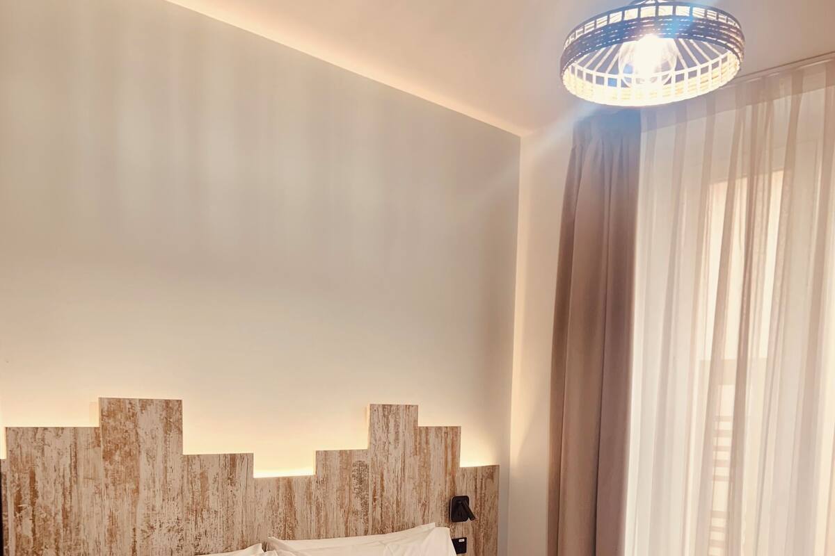 Quarto de hotel moderno com uma cama grande, cabeceira de madeira e luminária pendente.