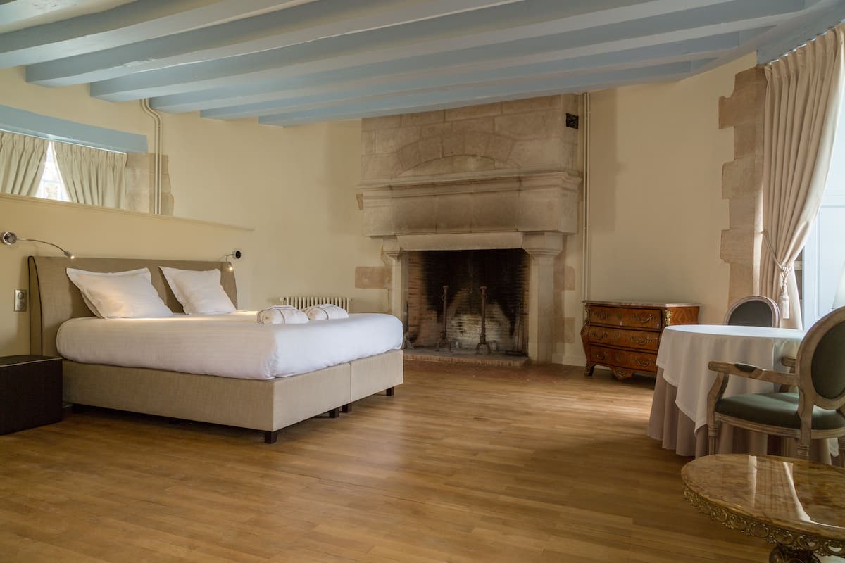 A bedroom with a bed, a fireplace, a dresser, a table, and a chair.
