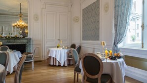 A dining area with wooden chairs and tables, a chandelier, and a view of the city through a window.